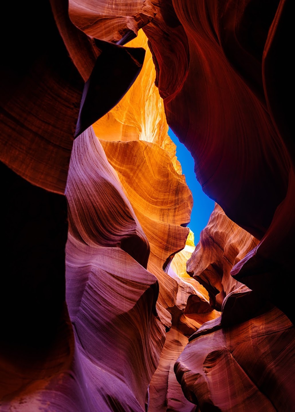 Orange and violet sandstone walls framing blue sky in a narrow canyon