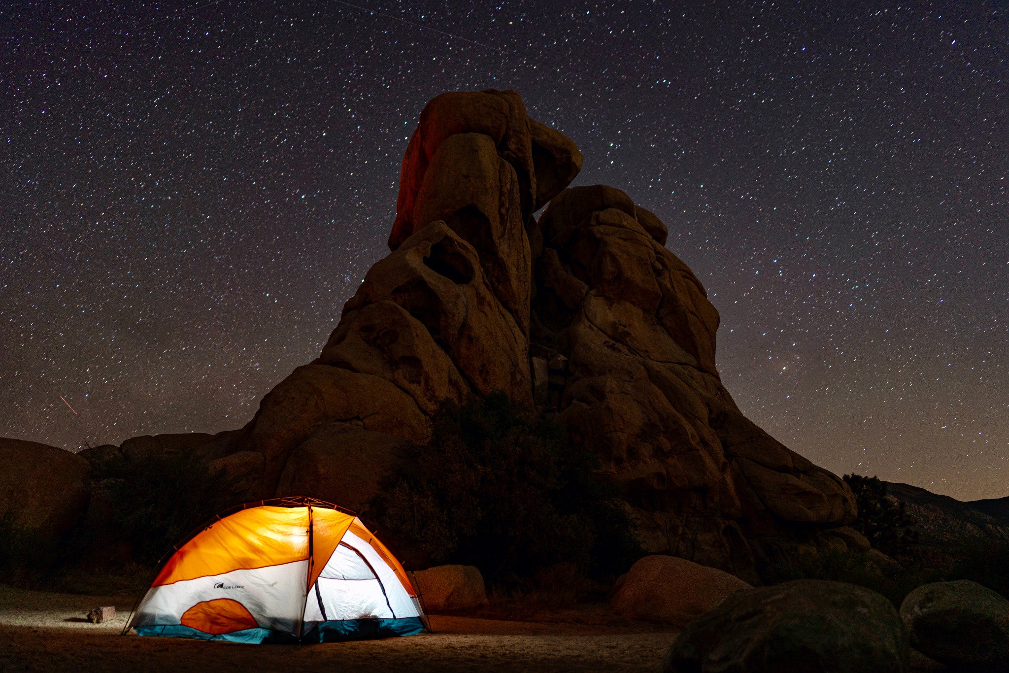 Glowing orange and white tent beneath towering desert rock formations and a sky filled with stars