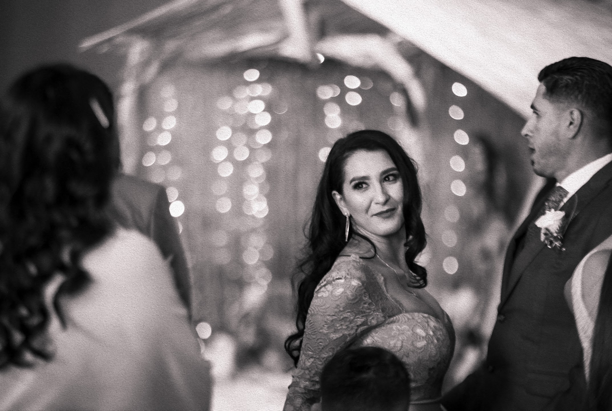 Black and white candid photograph of a woman turning toward the camera during a wedding celebration