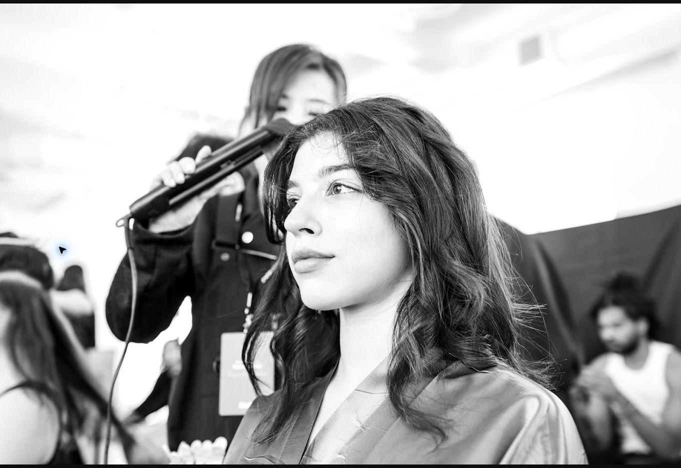 Black and white photograph of a woman having her hair styled backstage