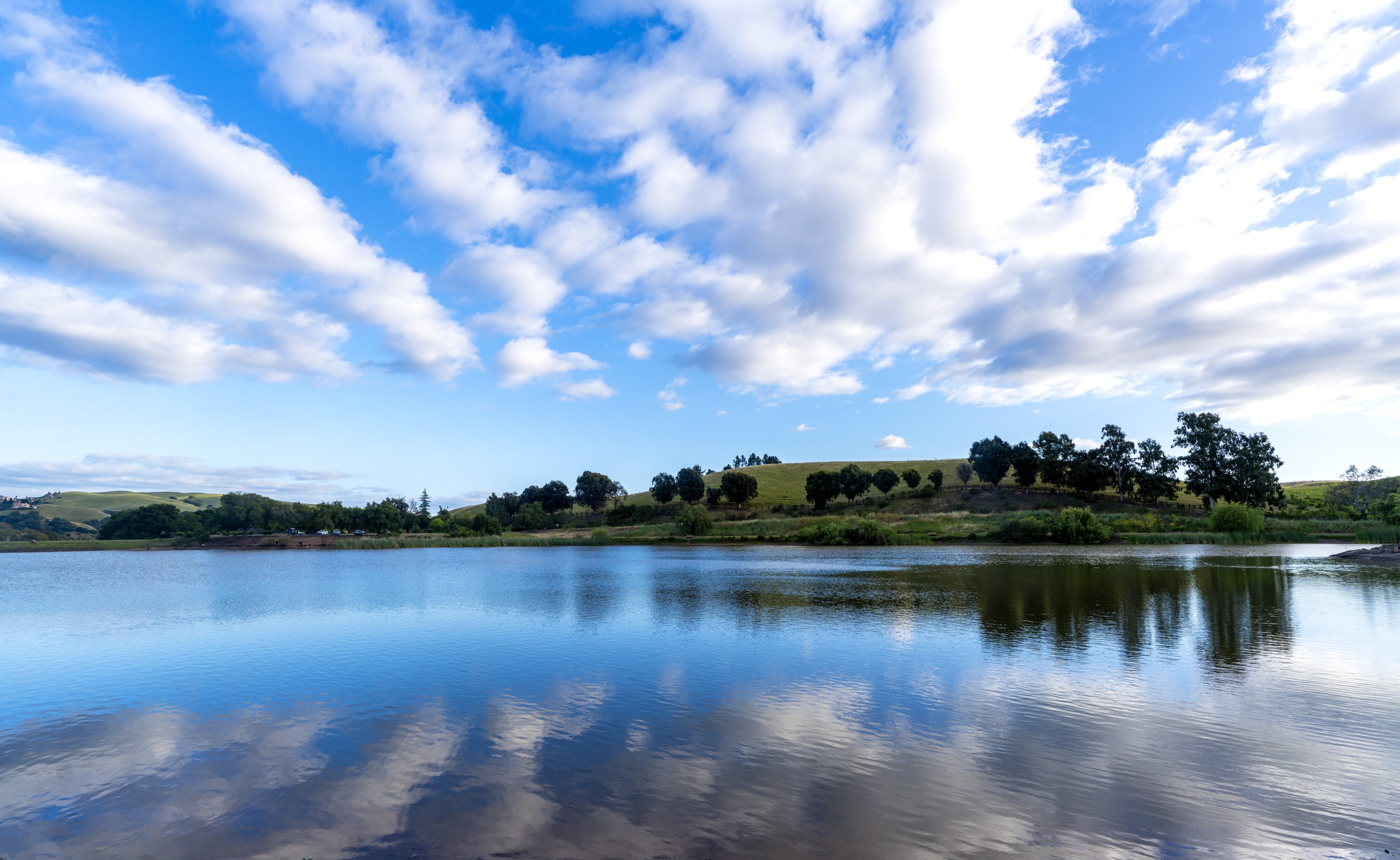 Cloud-filled blue sky mirrored in a lake bordered by green fields
