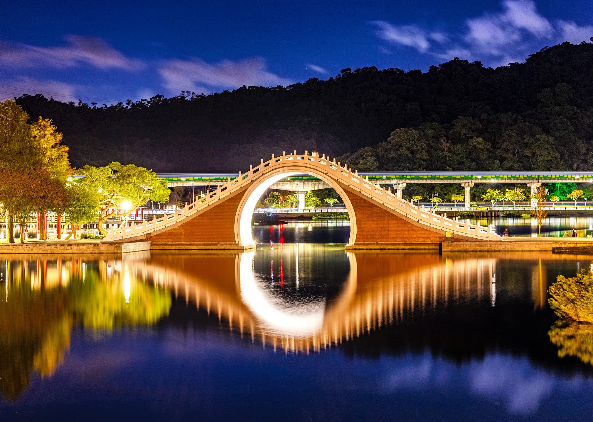 An illuminated arched bridge and its circular reflection in still water at night