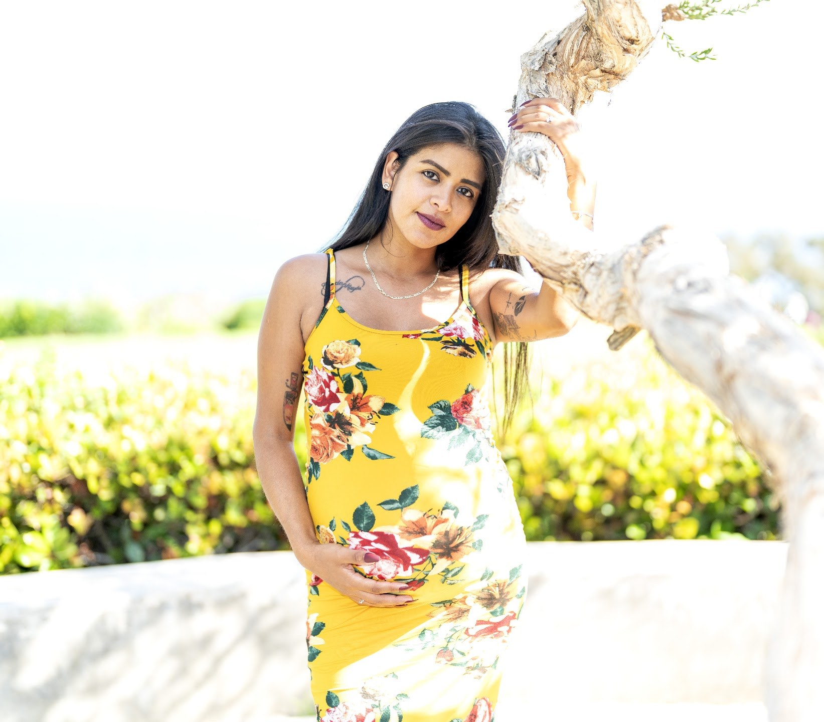 Reyna wearing a yellow floral dress beside a sunlit tree