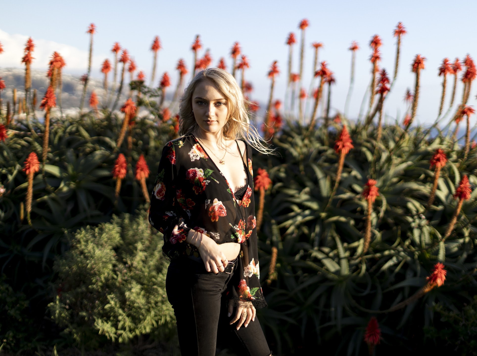Taylor wearing a dark floral blouse among red flowering aloes