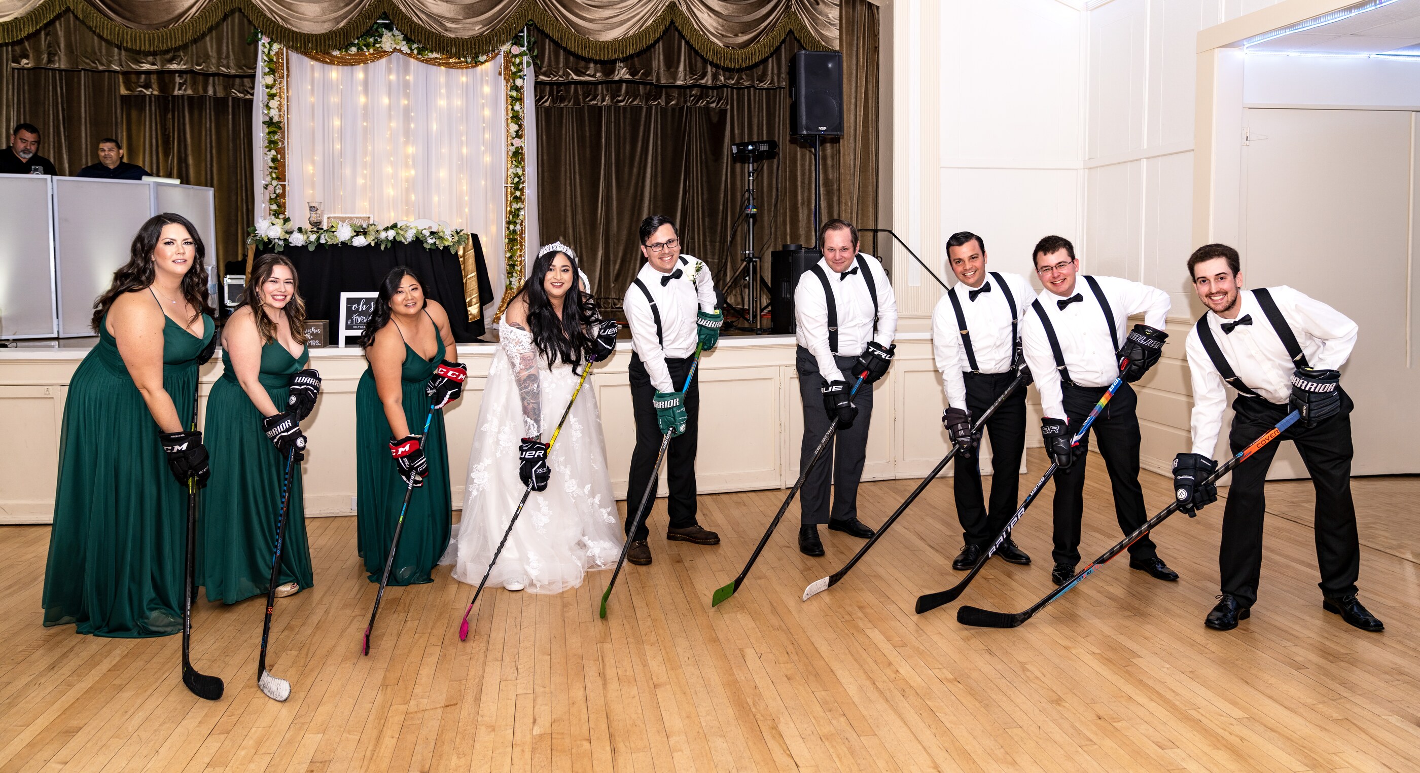 Bride, groom and wedding party posing with hockey sticks on the reception dance floor